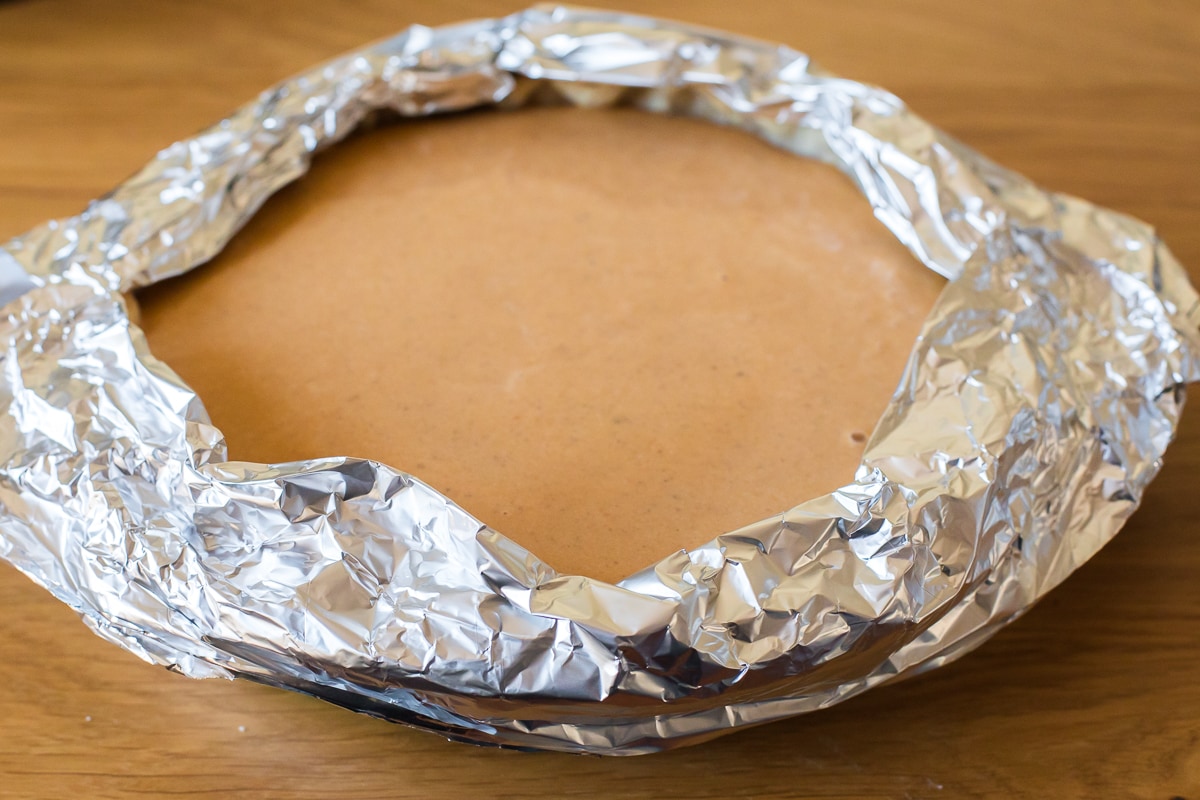 pie pan filled with pumpkin pie filling and tinfoil around it to prevent pie crust edges from burning.