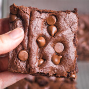 hand holding up a brownie with chocolate chips on top.