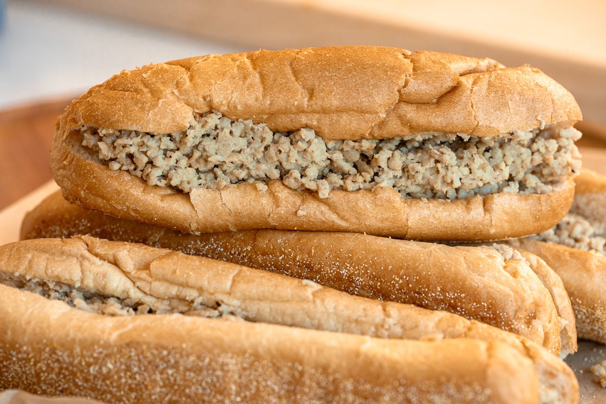 Side view of stacked chicken cheesesteaks on Amoroso rolls filled with ground chicken and Cooper Sharp cheese.