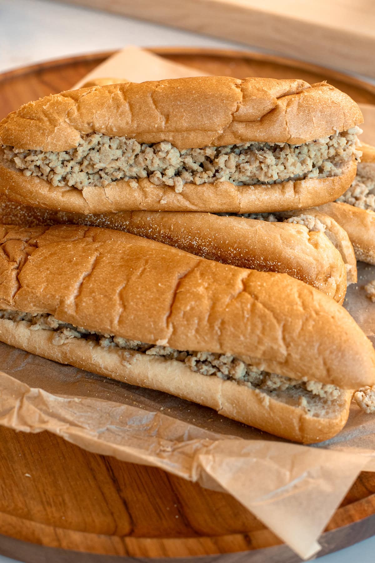 Chicken cheesesteak sandwiches stacked on a wooden board with parchment, filled with ground chicken and Cooper Sharp cheese.