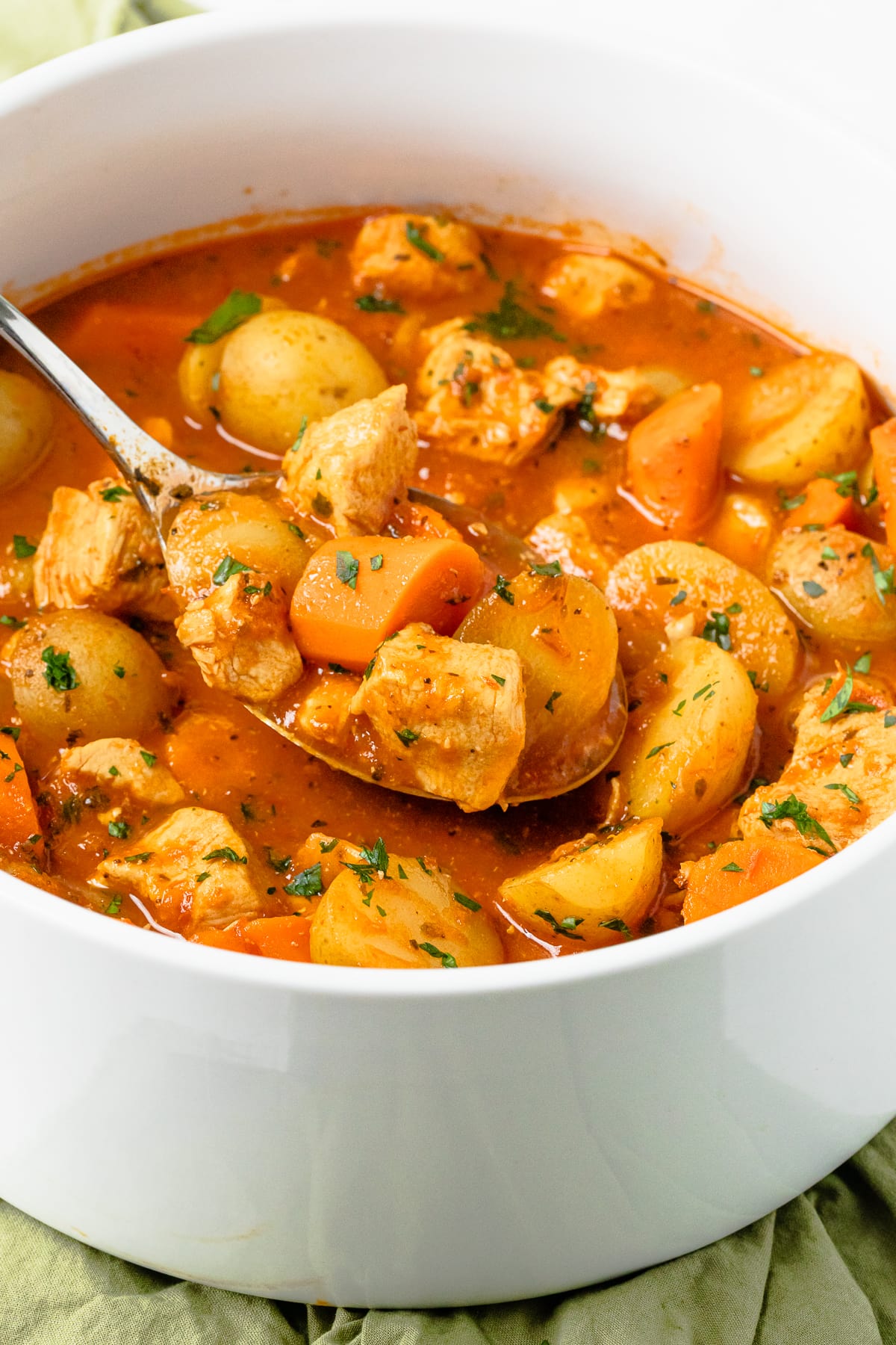 chicken stew with potatoes and carrots in a white pot with a spoon scooping some.