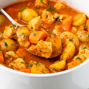chicken stew with potatoes and carrots in a white pot with a spoon scooping some.