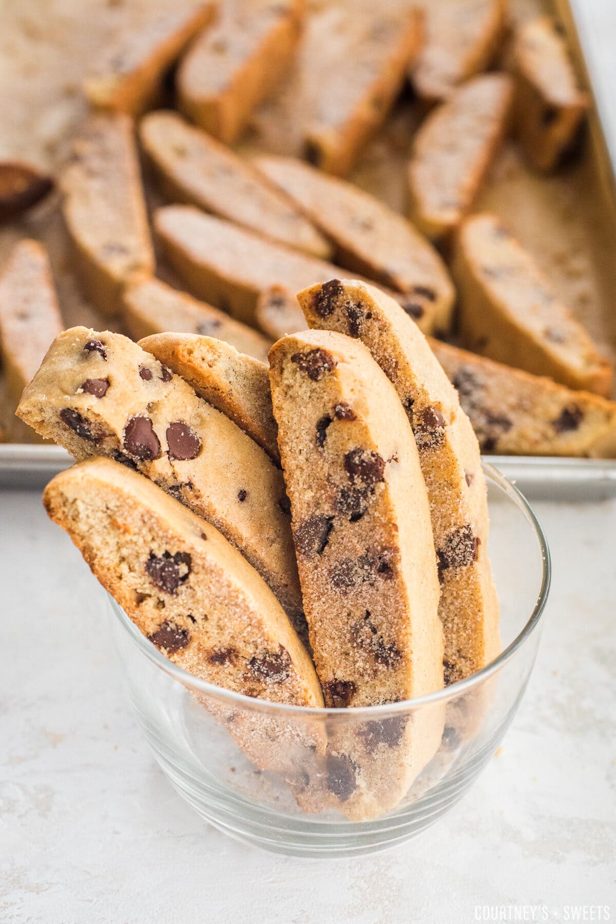 pieces of mandel bread in a glass bowl with mandel bread sliced on a sheet pan in the background