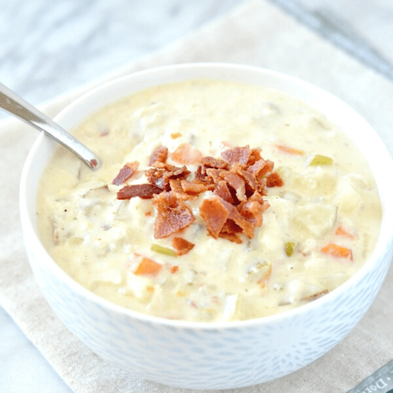seafood chowder with flounder fish with crumbled bacon on top in a white bowl with a spoon on a beige napkin.