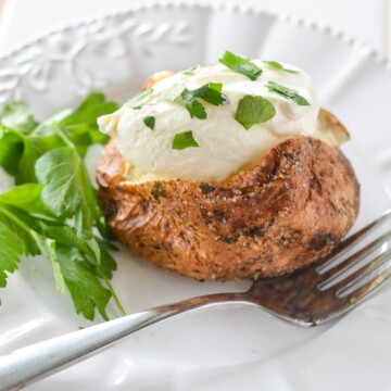 air fryer baked potato with sour cream and parsley garnish on a white plate.