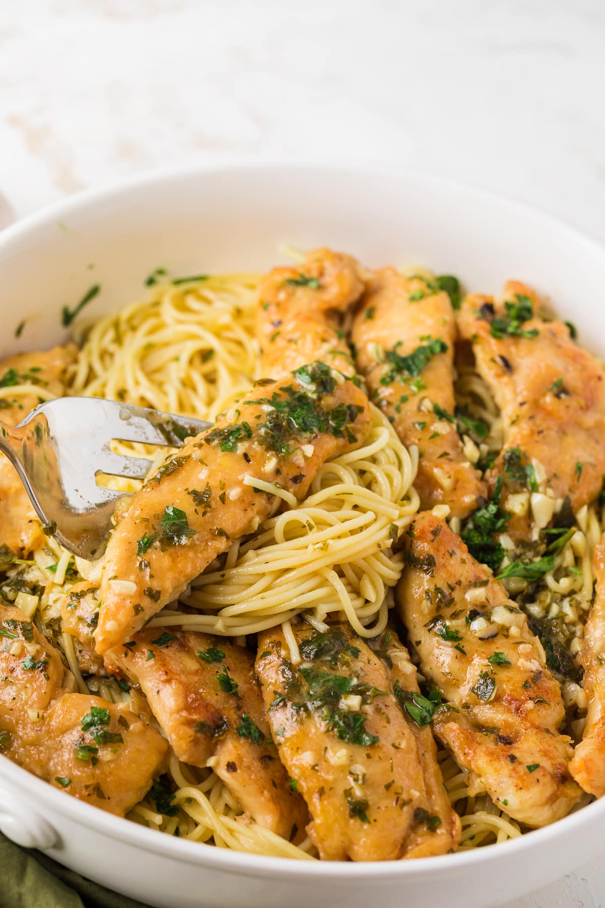 chicken scampi over pasta on a fork in a white bowl.
