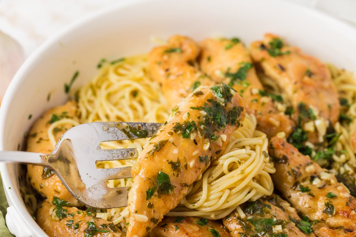 chicken scampi made with chicken tenderloins on a fork with pasta in a white serving dish.