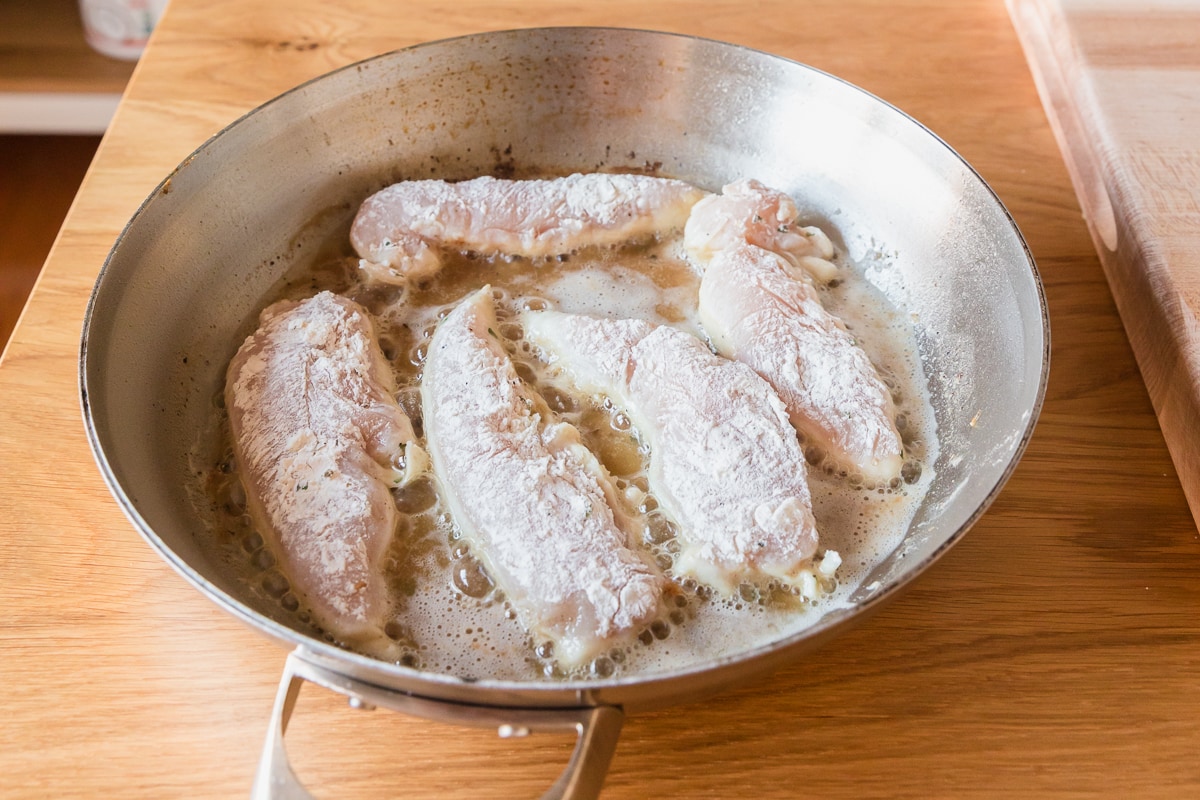 chicken tenderloins coated in flour being pan fried.