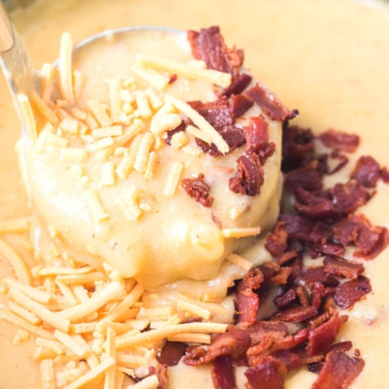 baked potato soup in a pot with a ladle with shredded cheddar cheese and crumbled bacon on top.