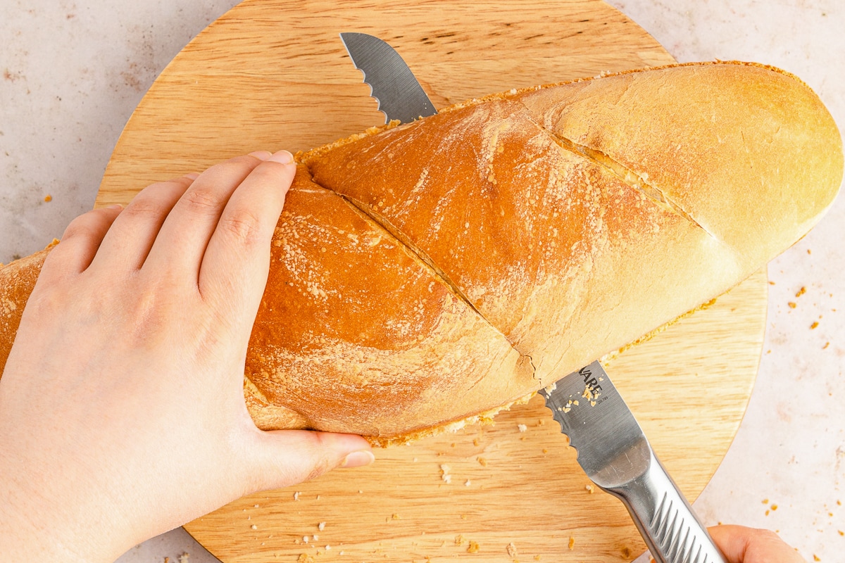hand slicing open French bread for garlic bread.