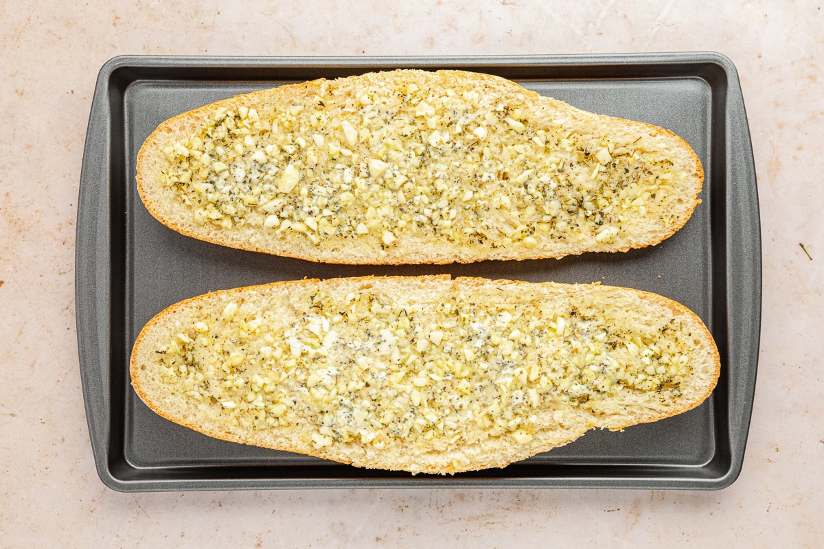 garlic bread spread on bread on a baking sheet ready to bake.