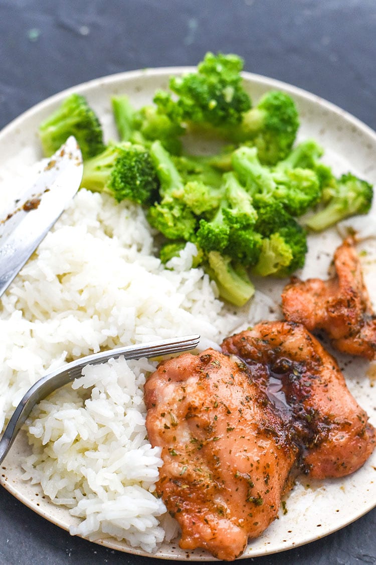 baked boneless skinless chicken thighs on a plate with rice and broccoli and a fork.