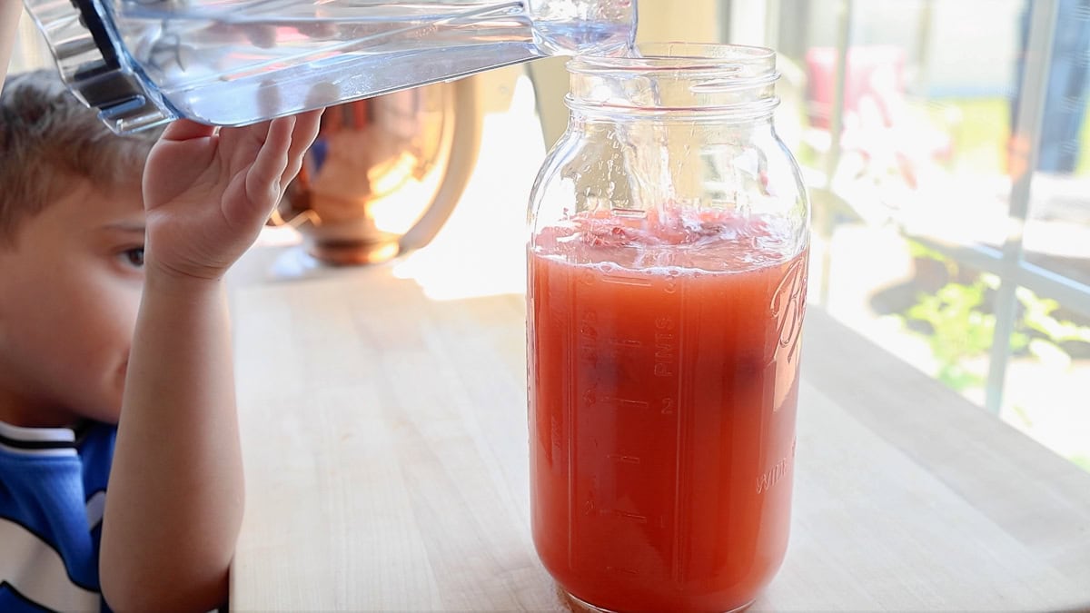 adding water to strawberry lemonade pitcher.