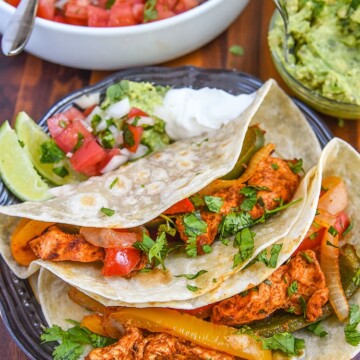 baked chicken fajitas wrapped in a tortilla on a plate with fajitas toppings.