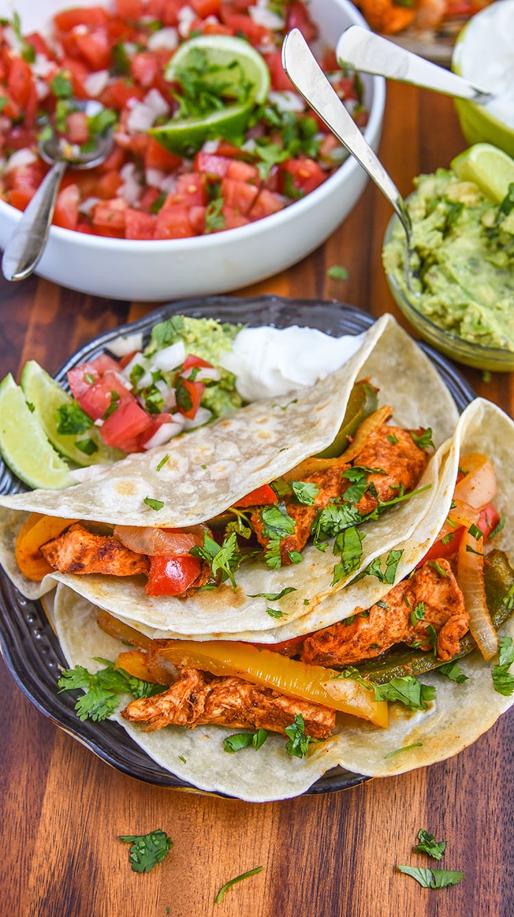 baked chicken fajitas wrapped in a tortilla on a plate with fajitas toppings.