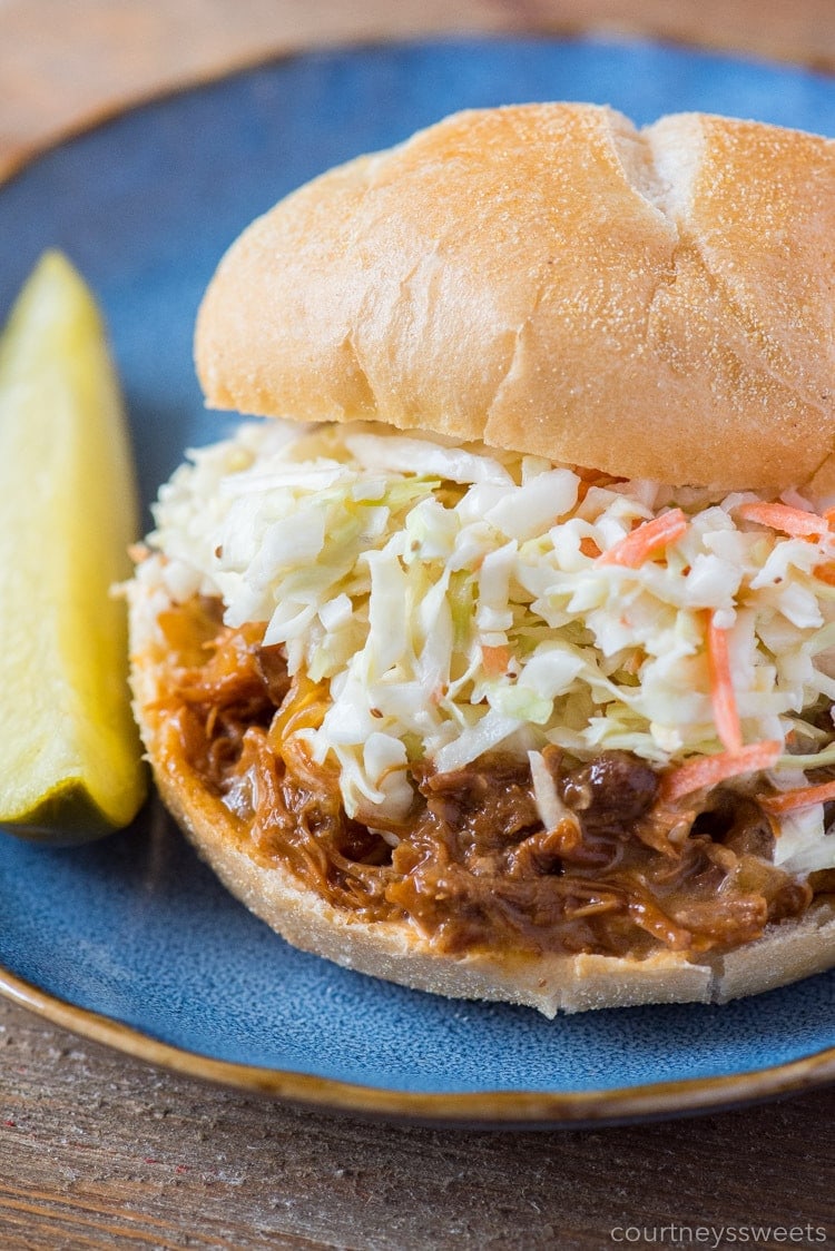 slow cooker bbq pulled pork sandwich with coleslaw on a kaiser roll and pickle on the side