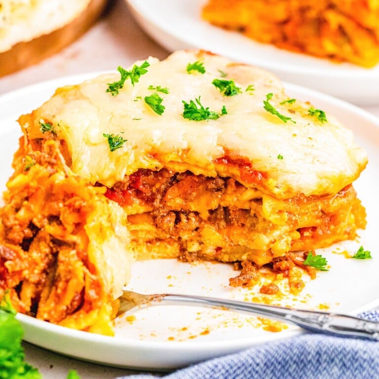 lasagna bolognese on a plate with a fork and bite full taken out of it.
