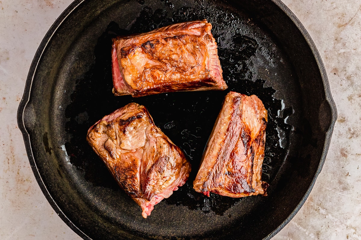 seared short ribs in a cast iron skillet.