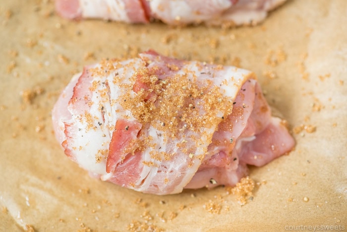 raw bacon wrapped chicken thighs on parchment paper with brown sugar seasoning mix