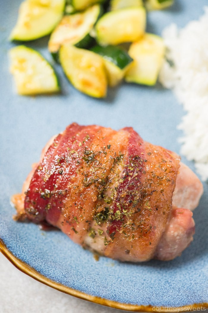 bacon wrapped chicken thighs on a plate with rice and sauteed zucchini