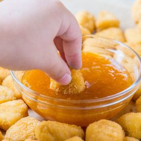 hand dipping chicken nuggets in sweet and sour sauce