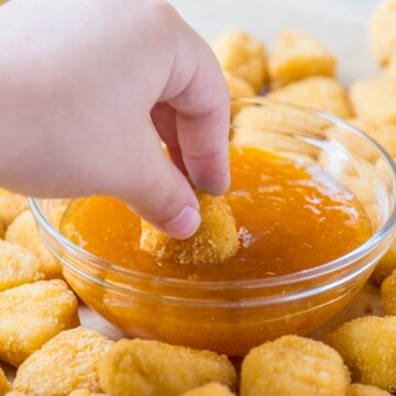 hand dipping chicken nuggets in sweet and sour sauce