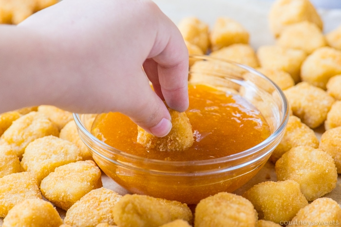 hand dipping chicken nuggets in sweet and sour sauce 