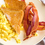 yellow plate with air fryer bacon, toast with butter, and scrambled eggs.