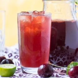 cherry limeade in a glass with ice and pitcher in background