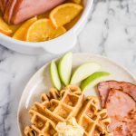 sweet potato waffles with ham steaks on a plate with sliced apples