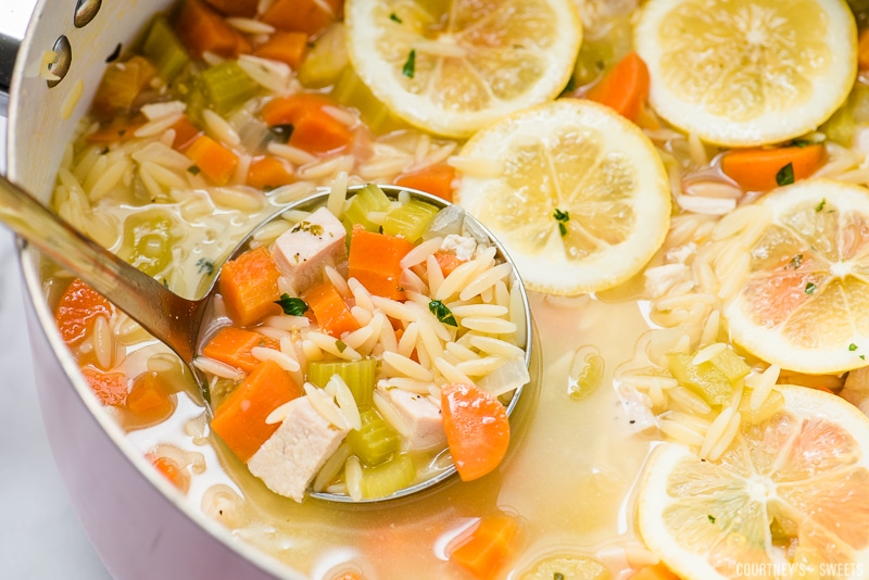 lemon chicken orzo soup in a pot with a ladle and fresh lemon slices