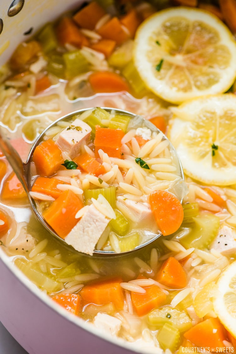 lemon chicken orzo soup in a ladle with pot