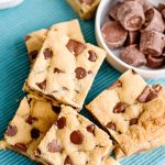 overhead photo of chocolate chip cookie bars with rolo candies in a bowl on a teal napkin