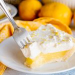 lemon pie with a fork in it on a plate with fresh lemons in background