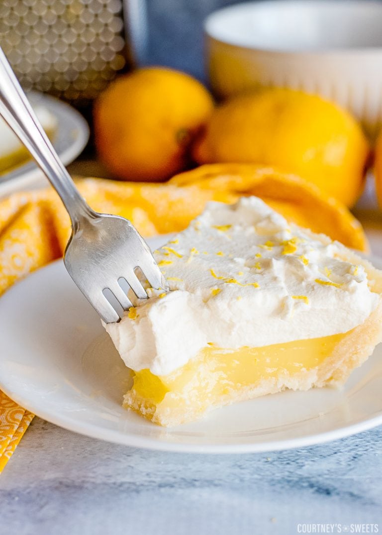 lemon pie with a fork in it on a plate with fresh lemons in background