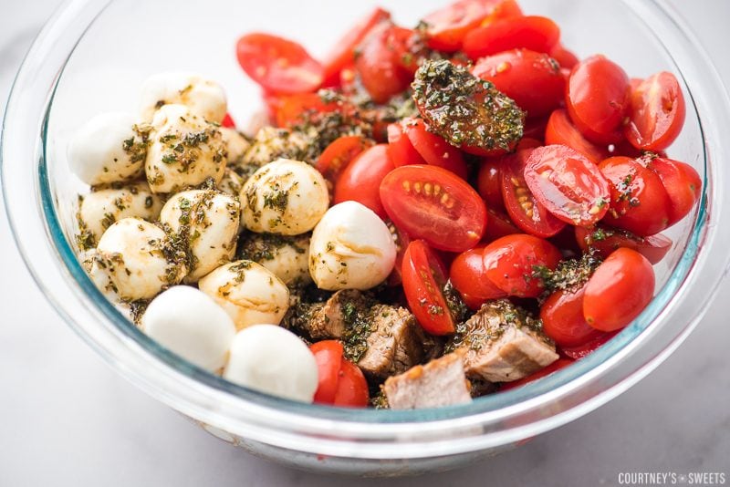 pork caprese salad in a glass bowl with dressing and herbs