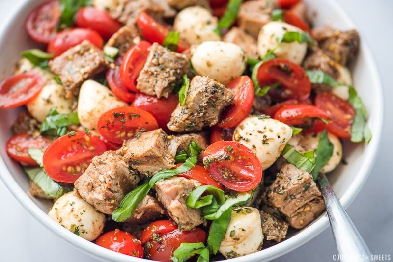 caprese salad with pork loin in a bowl with spoon, garnished with chiffonade of basil
