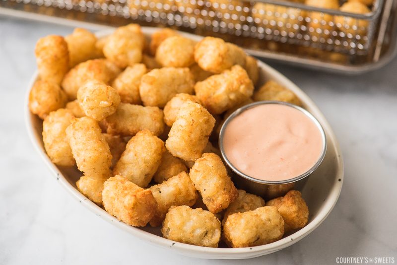 tater tots with fry sauce in dipping cup and air fryer basket in background