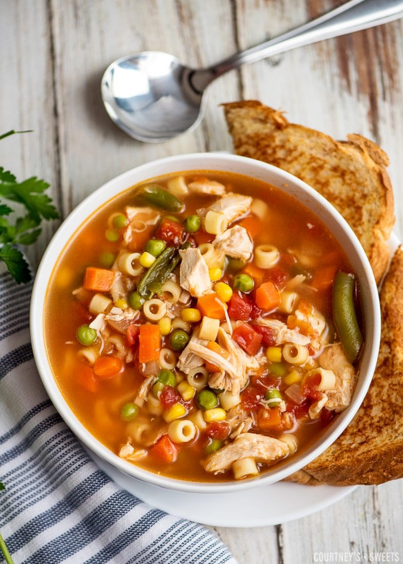 chicken vegetable soup in a white bowl with brea don a plate and spoon to the side
