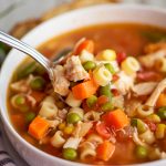 close up shot of chicken vegetable soup on a spoon in a white bowl