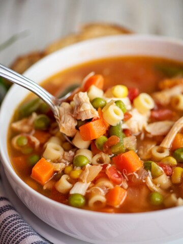 close up shot of chicken vegetable soup on a spoon in a white bowl