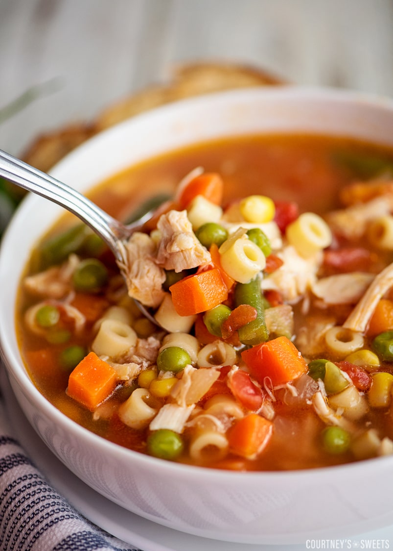 close up shot of chicken vegetable soup on a spoon in a white bowl