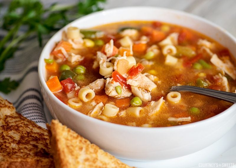 chicken vegetable soup in a bowl with a spoon and bread on plate