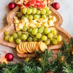 christmas tree cheese platter with fruit, cheese, and crackers chopped on a christmas tree shaped board with garland on the bottom for decoration