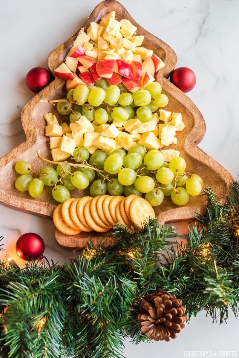 christmas tree cheese platter with fruit, cheese, and crackers chopped on a christmas tree shaped board with garland on the bottom for decoration