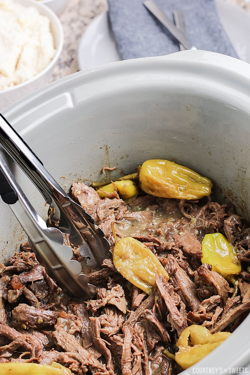 mississippi pot roast cooked in a gray slow cooker with tongs