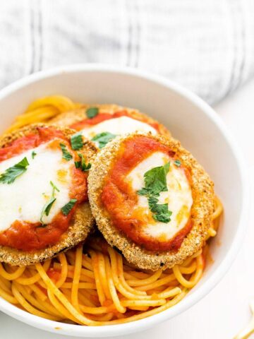 air fryer eggplant parmesan in a white bowl over spaghetti with sauce