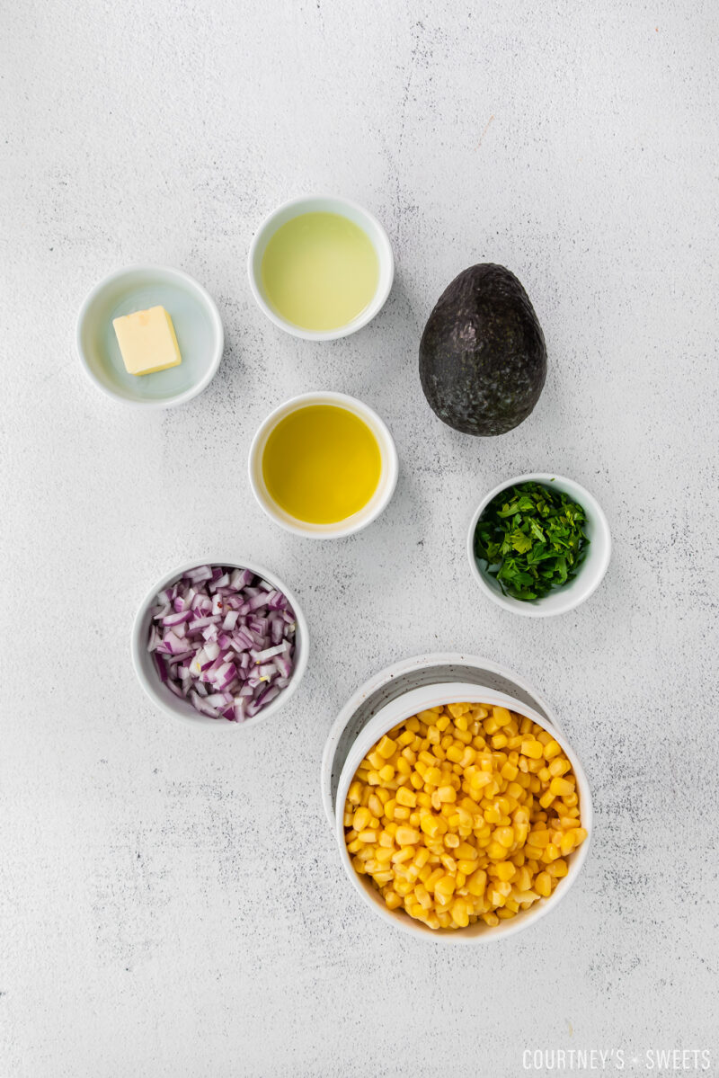 ingredients for avocado corn salsa in small bowls on cement backdrop