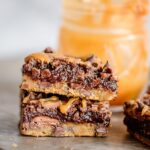 stacked brookies on sheet pan with jar of caramel in background