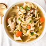 turkey noodle soup in a bowl with spoons to the left